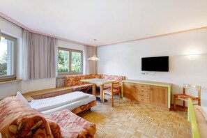 A room with two beds, a dining table, a TV, and a window with curtains. - Apartment '1 Residence Ciasa Ulli Typ B' with Mountain View, Shared Terrace and Wi-Fi (San Cassiano)