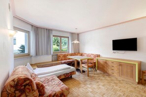 Ein Zimmer mit einem Bett, einem Sofa, einem Esstisch mit Stühlen, einem Fernseher und einem Fenster mit Vorhängen.
