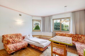 A room with a bed, a sofa, a table, and a chair. There are windows with curtains, a radiator, and a ceiling light fixture. - Apartment '1 Residence Ciasa Ulli Typ B' with Mountain View, Shared Terrace and Wi-Fi (San Cassiano)