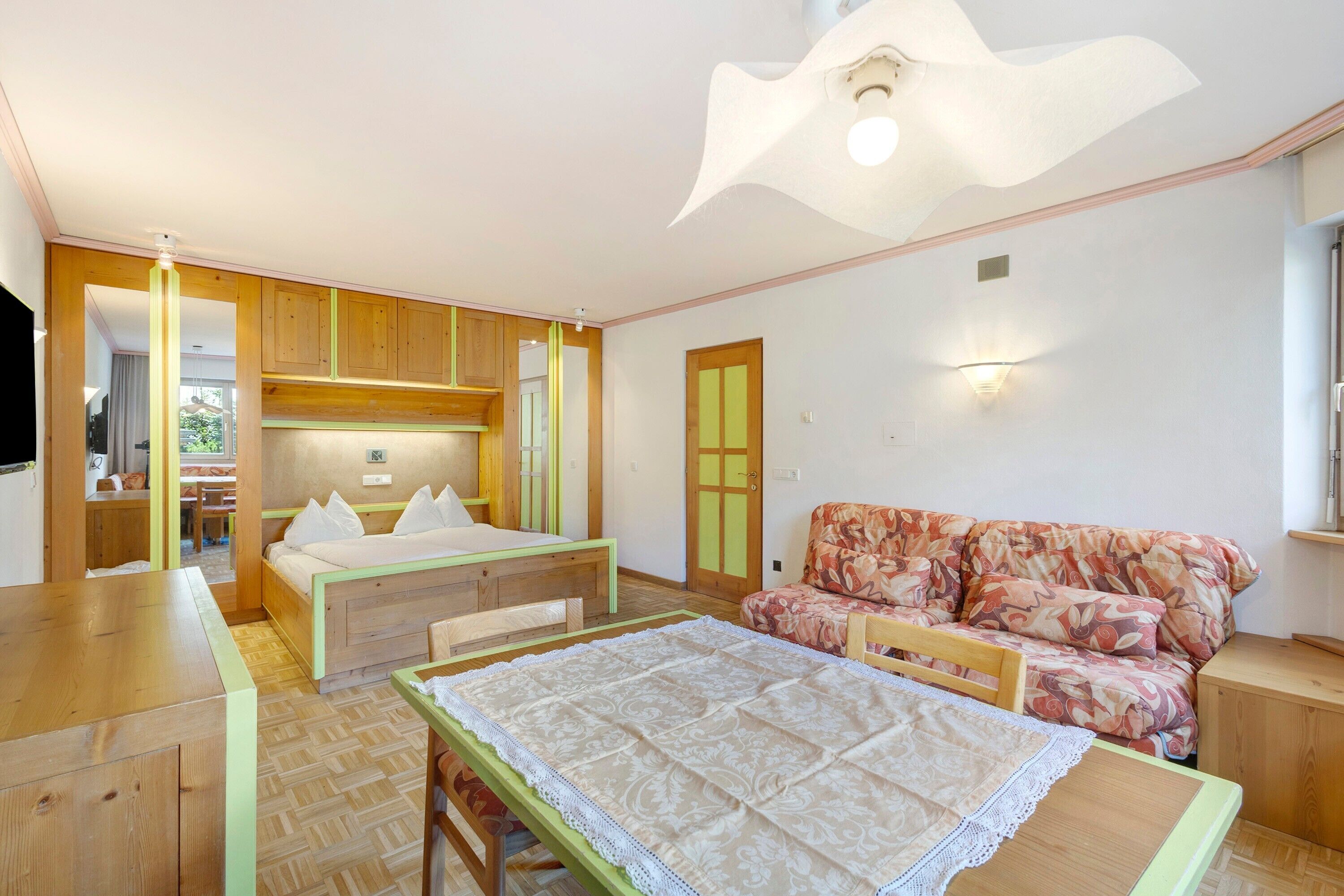 Een kamer met een bed, een slaapbank, een tafel en een kitchenette.
