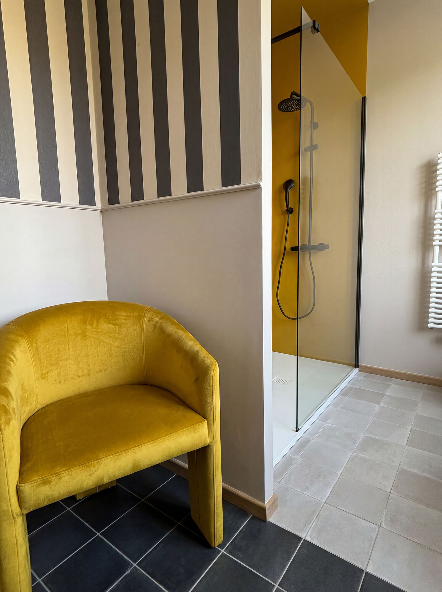 Una stanza con un divano giallo, un angolo doccia con porta in vetro e decorazioni murali a righe.
