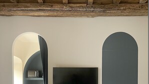 Un dormitorio con cama, televisor montado en la pared y un arco que da a una zona de cocina.