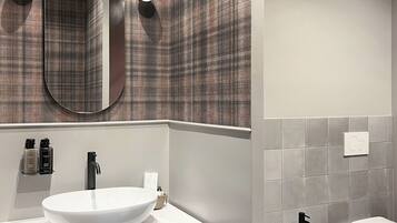 Un bagno moderno con uno specchio grande, due luci a parete, un lavandino bianco, un rubinetto nero, un water bianco e un bidet.