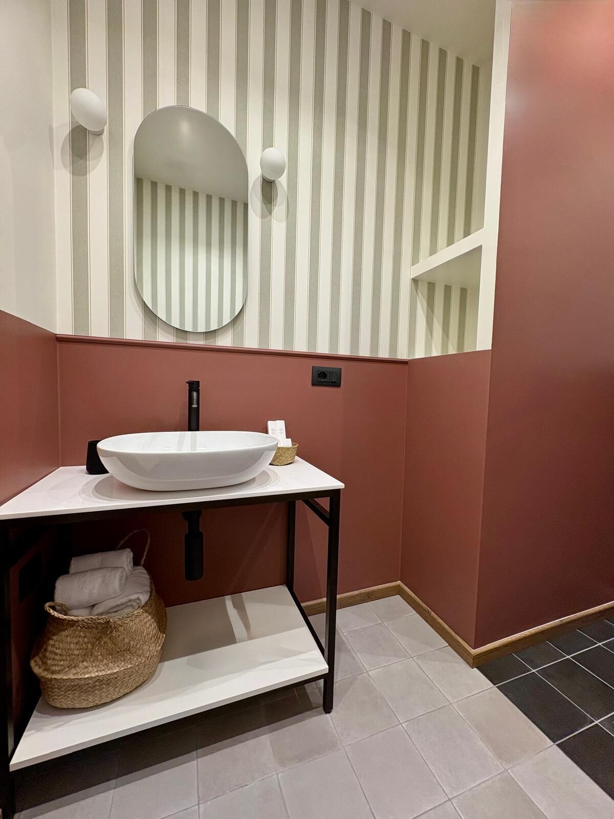 Een badkamer met een wit wastafel, een ronde spiegel, gestreepte behang en een rode wand.