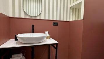 Een badkamer met een wit wastafel, een ronde spiegel, gestreepte behang en een rode wand.