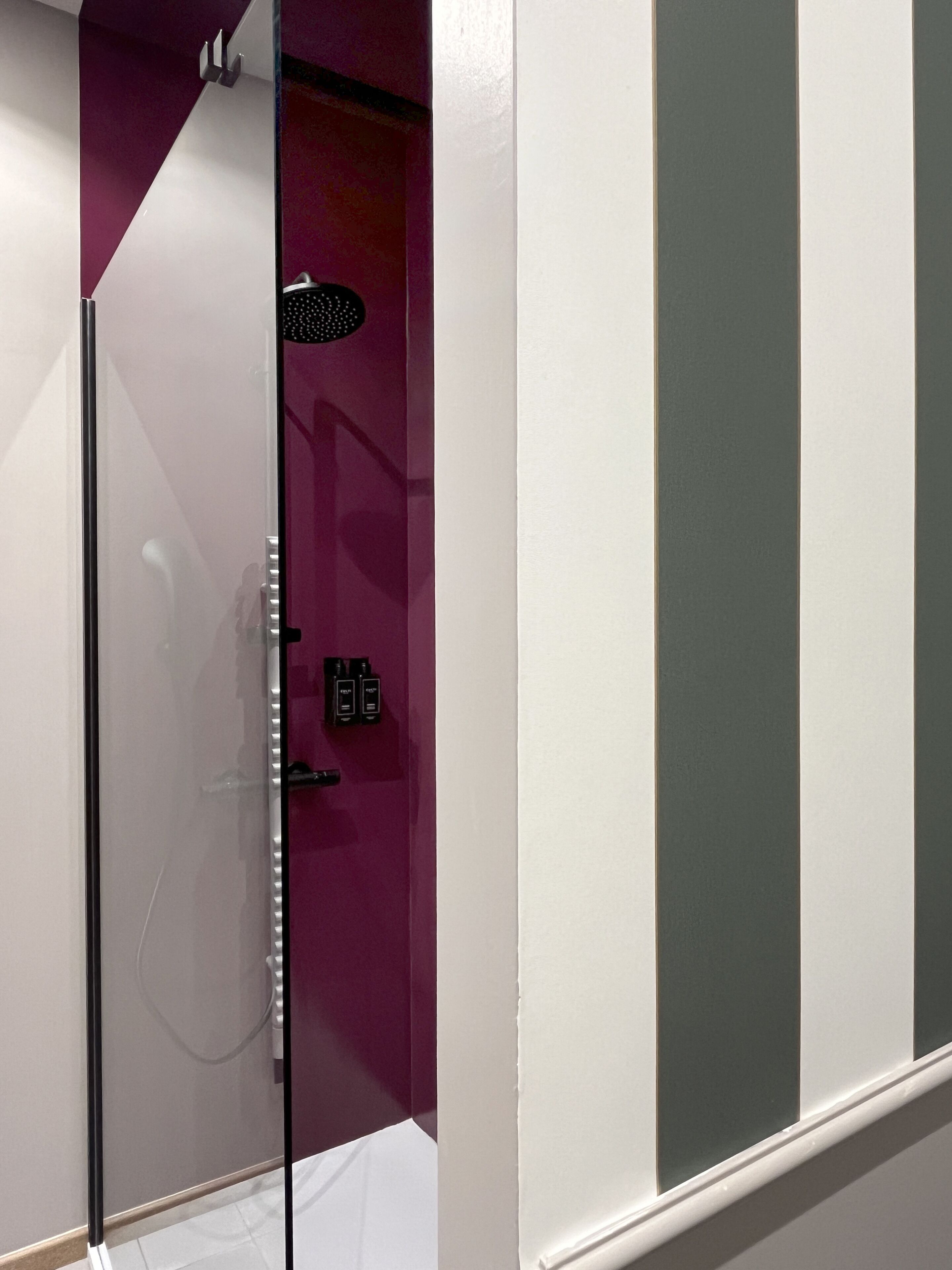 A bathroom with a glass shower enclosure, a purple accent wall, and a white door.