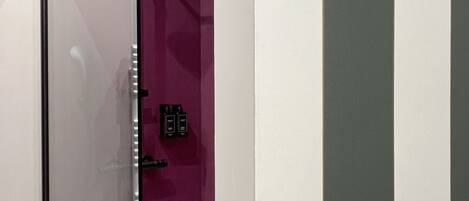 A bathroom with a glass shower enclosure, a purple accent wall, and a white door.