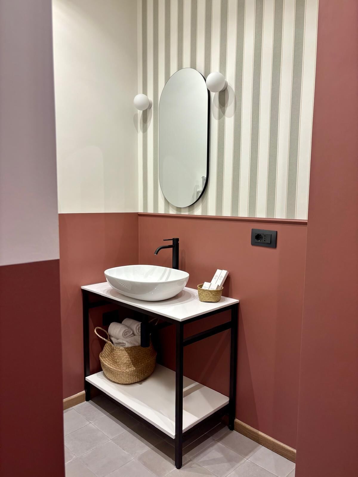 A bathroom with a white vessel sink, a black faucet, a mirror, and striped wallpaper.