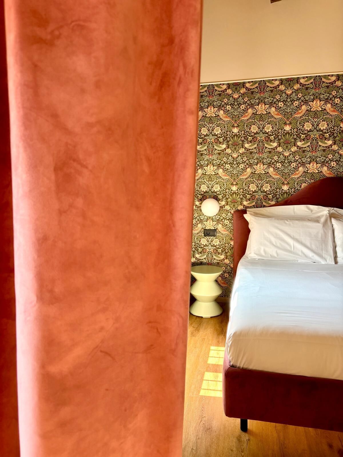 A bed with white bedding, a patterned wallpaper, and a bedside table with a lamp.