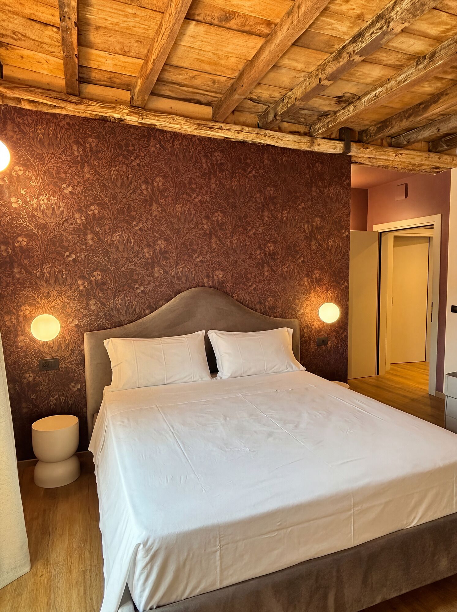 A bedroom with a wooden ceiling, a bed with white bedding, and two wall-mounted lights.