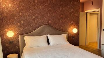 A bedroom with a wooden ceiling, a bed with white bedding, and two wall-mounted lights.