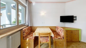 A corner room with a table, bench seating, a radiator, a TV, and a window. - Apartment 'Residence Ciasa Ulli Typ A' (San Cassiano)
