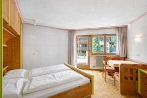 Une pièce comprenant un lit, une chaise, une table et une fenêtre donnant sur des immeubles et des arbres.