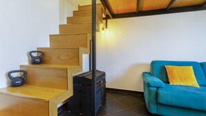A staircase with wooden steps and a black metal railing, a blue sofa with a yellow pillow, and kettlebells on the landing.