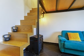 A staircase with wooden steps and a black metal railing, a blue sofa with a yellow pillow, and kettlebells on the landing.
