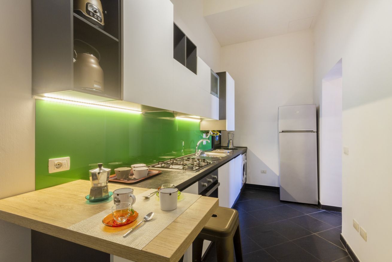 A compact kitchen with a green backsplash, a gas stove, a refrigerator, and a sink.