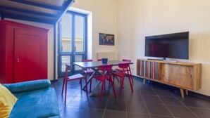 A room with a sofa, a dining table with chairs, a TV on a wooden stand, and a red cabinet.