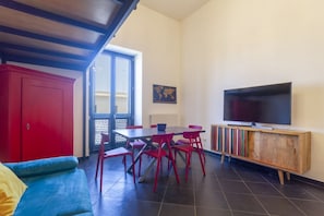 A room with a sofa, a dining table with chairs, a TV on a wooden stand, and a red cabinet.