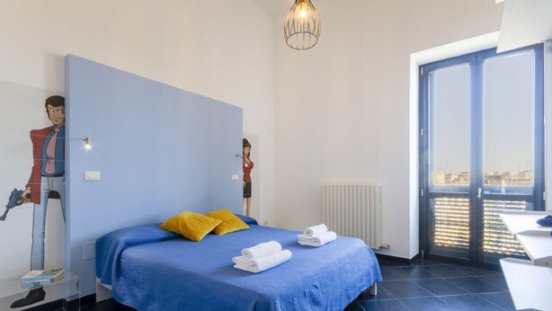 A hotel room with a bed, a large window, a radiator, and a ceiling light fixture.