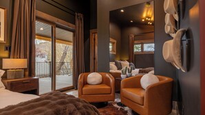 Een moderne slaapkamer met een groot bed, twee fauteuils, een bank, een open haard en uitzicht op het groen.