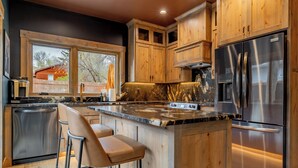Een moderne keuken met houten kastjes, een roestvrijstalen koelkast en een marmeren aanrecht.