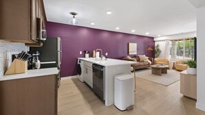Une cuisine moderne dotée d’un îlot central, un coin repas avec un canapé et des fauteuils, et un salon avec une table basse.