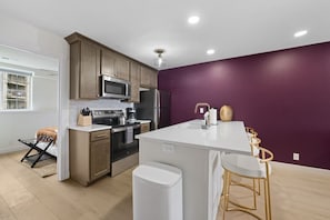 A modern kitchen with wooden cabinets, stainless steel appliances, and a purple accent wall.