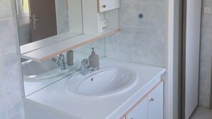 A bathroom with a double sink, a mirror, and a door leading to another room.