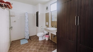 Et badeværelse med bruser, toilet, vask og et mørkt træskab.
