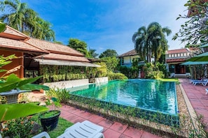 Ein Pool mit gefliestem Deck, umgeben von üppiger Vegetation und Palmen.
