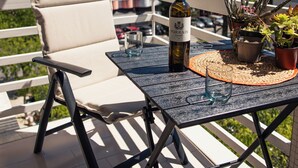 Un balcone con un tavolo, una sedia, una bottiglia di vino e piante in vaso.