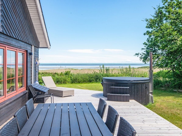 A deck with a table and chairs, a hot tub, and a view of the beach. - 4 Star Holiday Home in Hadsund (Hadsund)
