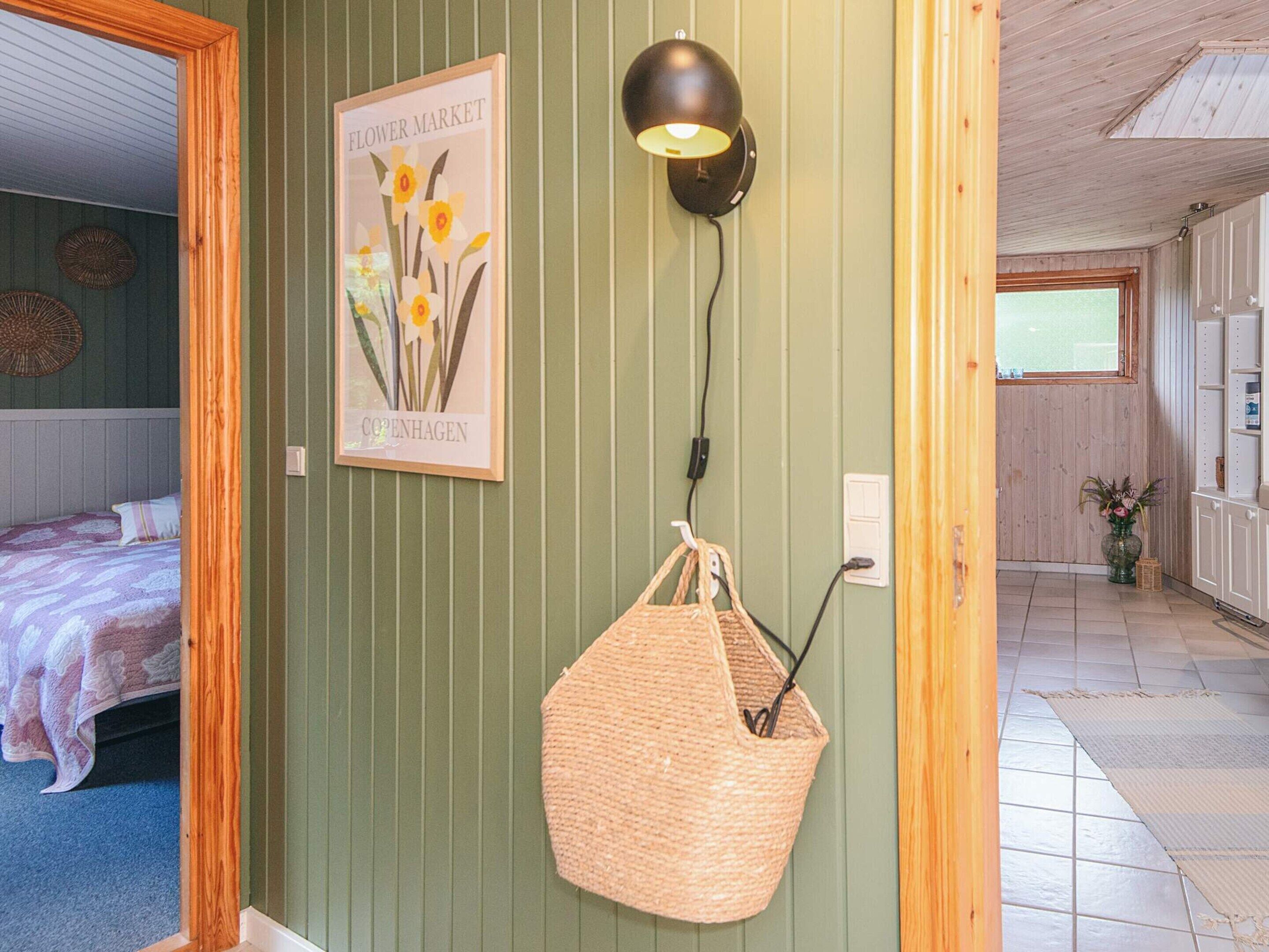 A room with a bed, a wall-mounted lamp, a framed picture, and a woven basket.
