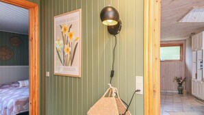 Una habitación con una cama, una lámpara de pared, un cuadro enmarco y una cesta de mimbre.