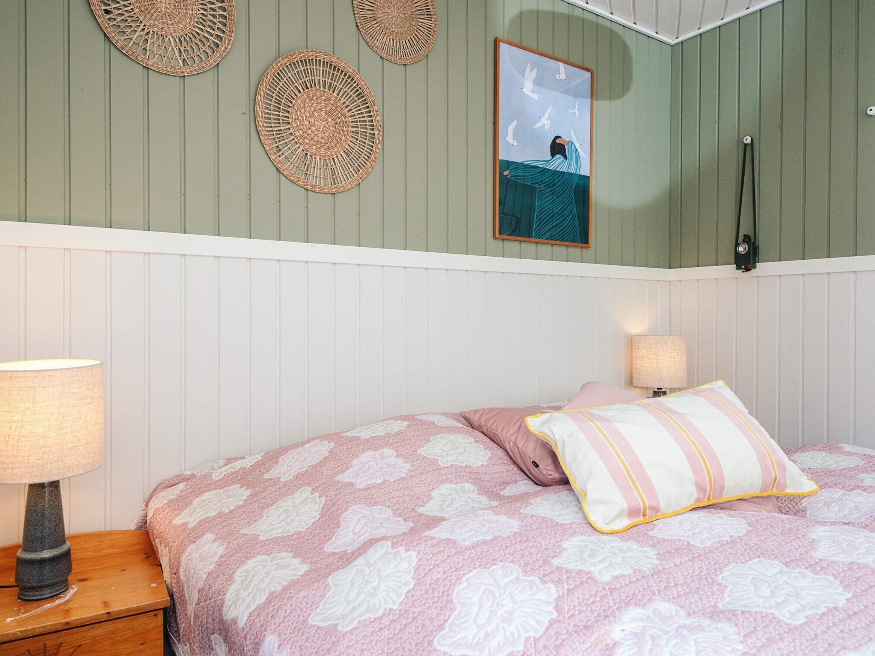 A bedroom with a bed, two bedside lamps, a wall-mounted clock, and three woven wall hangings.