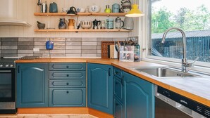 Una cocina con armarios verde azulado, encimera de madera, estufa integrada, un fregadero y una ventana con vista a follaje.