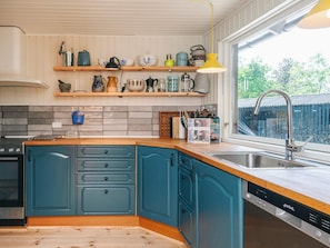 A kitchen with teal cabinets, a wooden countertop, a built-in stove, a sink, and a window with a view of greenery. - 4 Star Holiday Home in Hadsund (Hadsund)