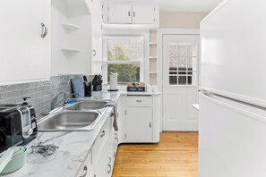 Cocina compacta con armarios blancos, encimera de mármol, barra para café y lavavajillas.