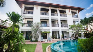 A multi-story hotel with a swimming pool, outdoor seating, and a well-maintained garden.