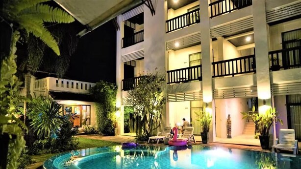 A swimming pool with lounge chairs and a building with balconies.