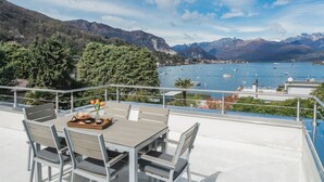 Una terraza con mesa y sillas con vistas a un lago con barcos, rodeada de montañas.