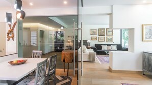 Un interior moderno con comedor, sala de estar con sofá y mesa de centro, y un separador de vidrio que delimita los espacios.