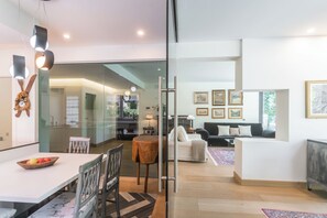 A modern interior with a dining area, a living room with a sofa and a coffee table, and a glass partition separating the spaces. - Villa Chiara - Four Bedroom Villa, Sleeps 8 (Stresa)