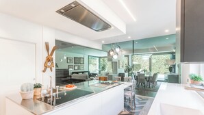 Cocina moderna con una isla central, zona de comedor con sillas y vistas al exterior.