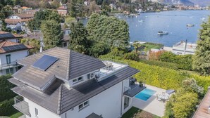 Una casa moderna de dos pisos con un panel solar en la azotea, una piscina y vista a un lago con barcos.