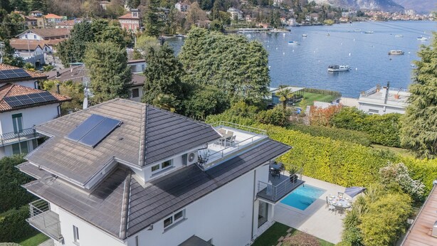 Ein modernes, zweistöckiges Haus mit einer Dachsolaranlage, einem Swimmingpool und Blick auf einen See mit Booten.