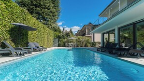 Ein Schwimmbad mit Liegestühlen und Sonnenschirmen, umgeben von Grünflächen und moderner Architektur.
