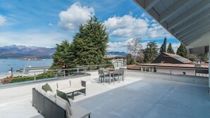 Eine Dachterrasse mit Außenmöbeln, Blick auf einen See, Berge und einen klaren Himmel.