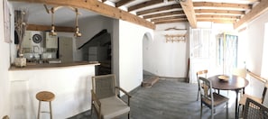 Eine rustikale Küche mit Holzbalkendecke, einem Essbereich mit rundem Tisch und Stühlen sowie einer Treppe, die zu einem weiteren Raum führt.
