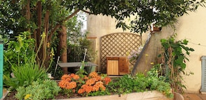 Ein Garten mit Holztisch und -stühlen, einer Gittertür und unterschiedlichen Pflanzen.